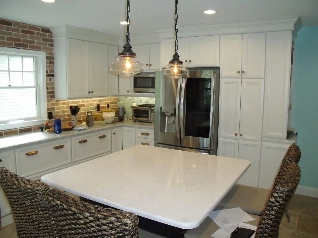 Bright white kitchen with island, pendant lights, stainless fridge, and white cabinetry