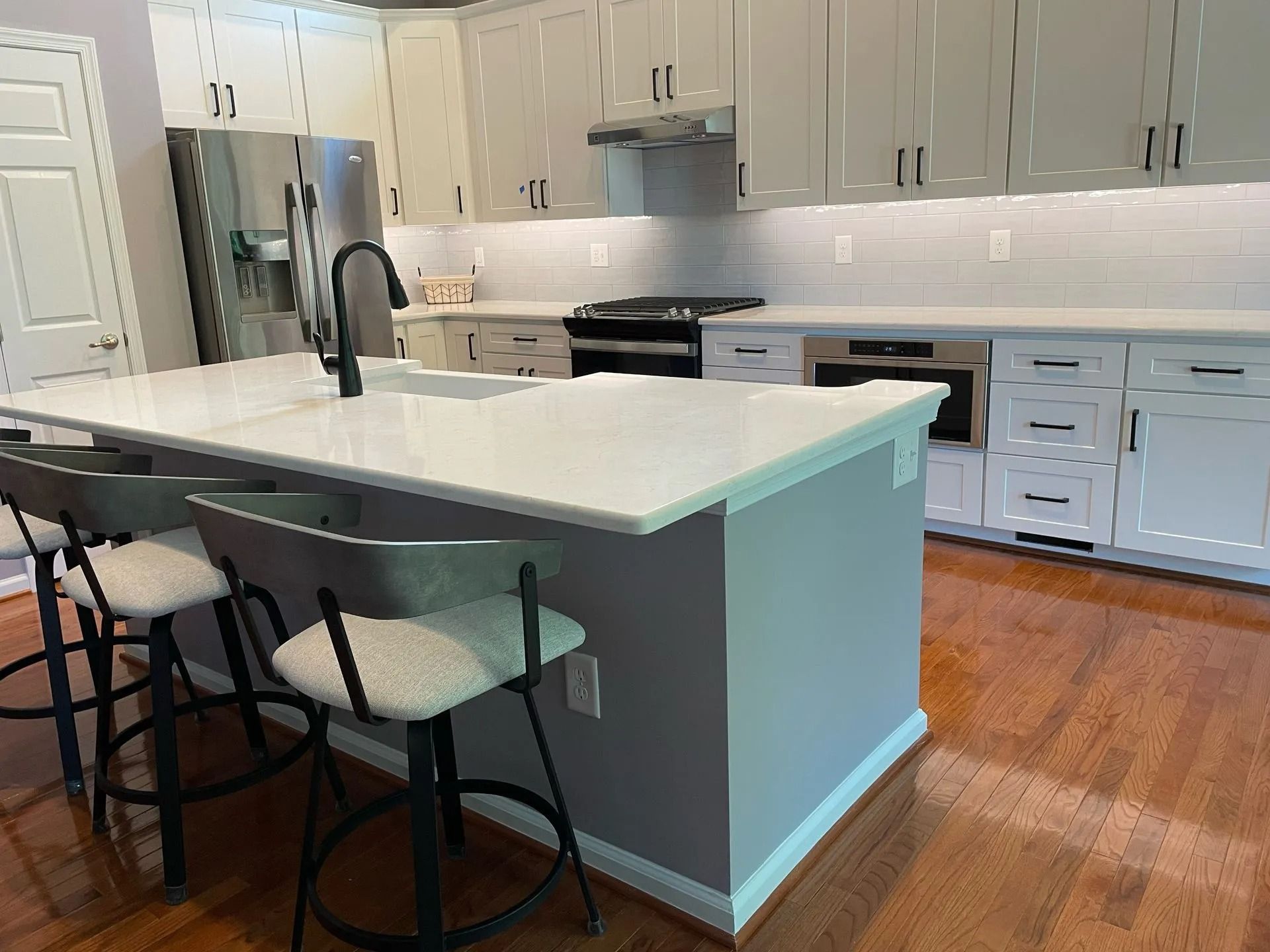 Modern kitchen with white cabinets, gray island, bar stools, and hardwood floors