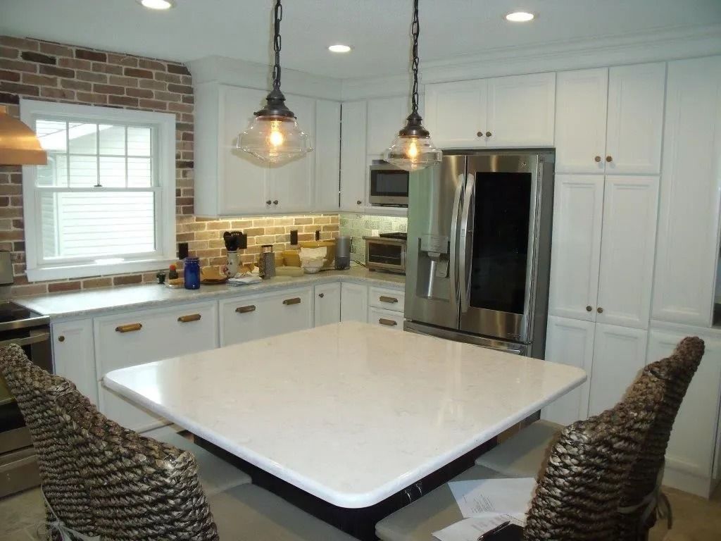 Bright kitchen with white cabinets, large island, stainless steel fridge, and woven barstools