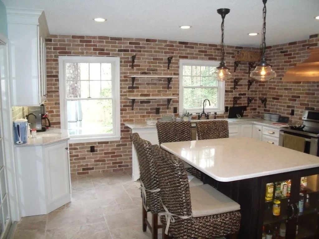 Bright kitchen with brick walls, white cabinets, and a large island under pendant lights