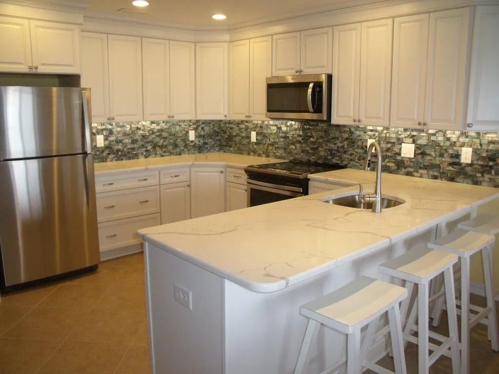 Modern kitchen with white cabinets, stainless steel appliances, marble island, and bar stools