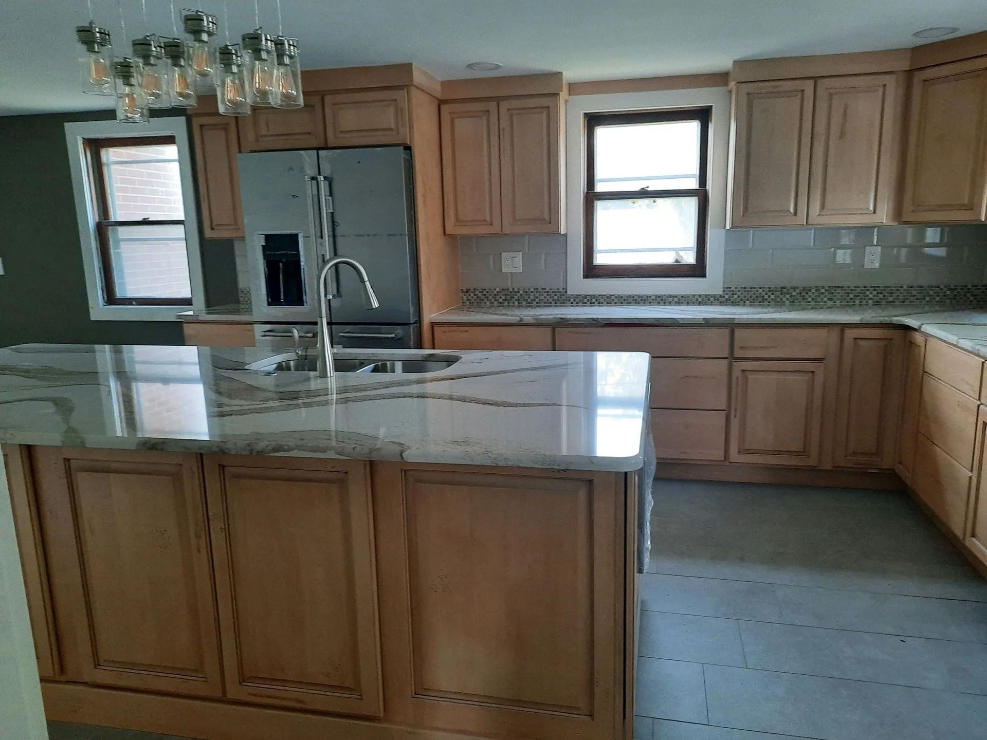 Modern kitchen with wood cabinets, granite island, stainless fridge, and large windows