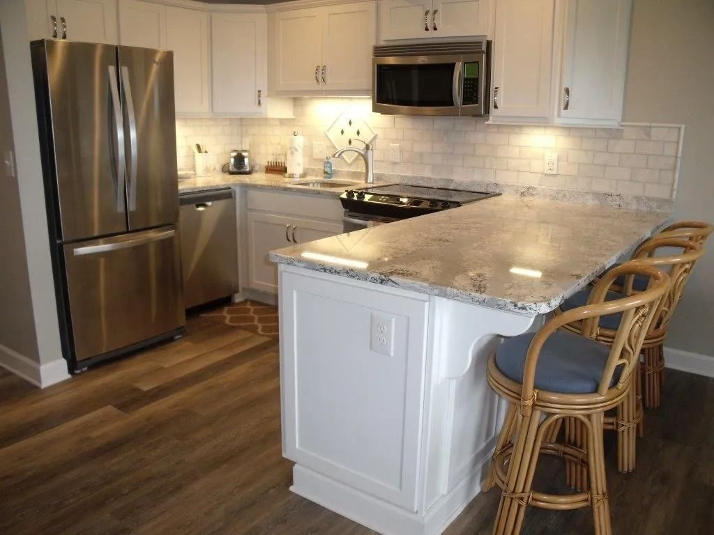 Bright modern kitchen with stainless steel appliances, white cabinets, island, and wicker bar stools.