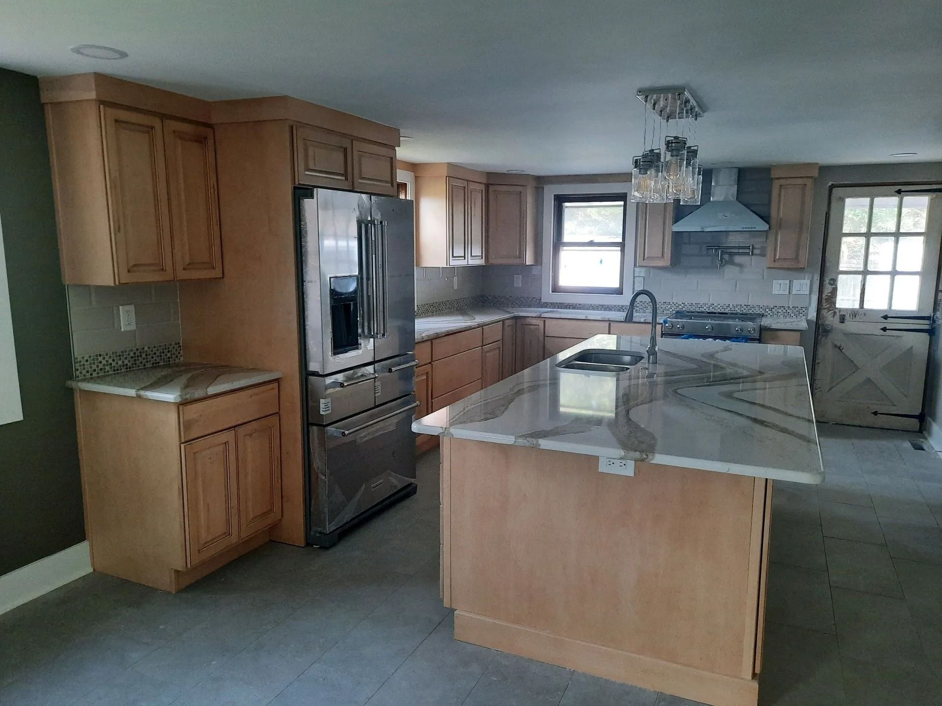 Empty kitchen with wood cabinets, stainless fridge, and a large island with marble countertop.