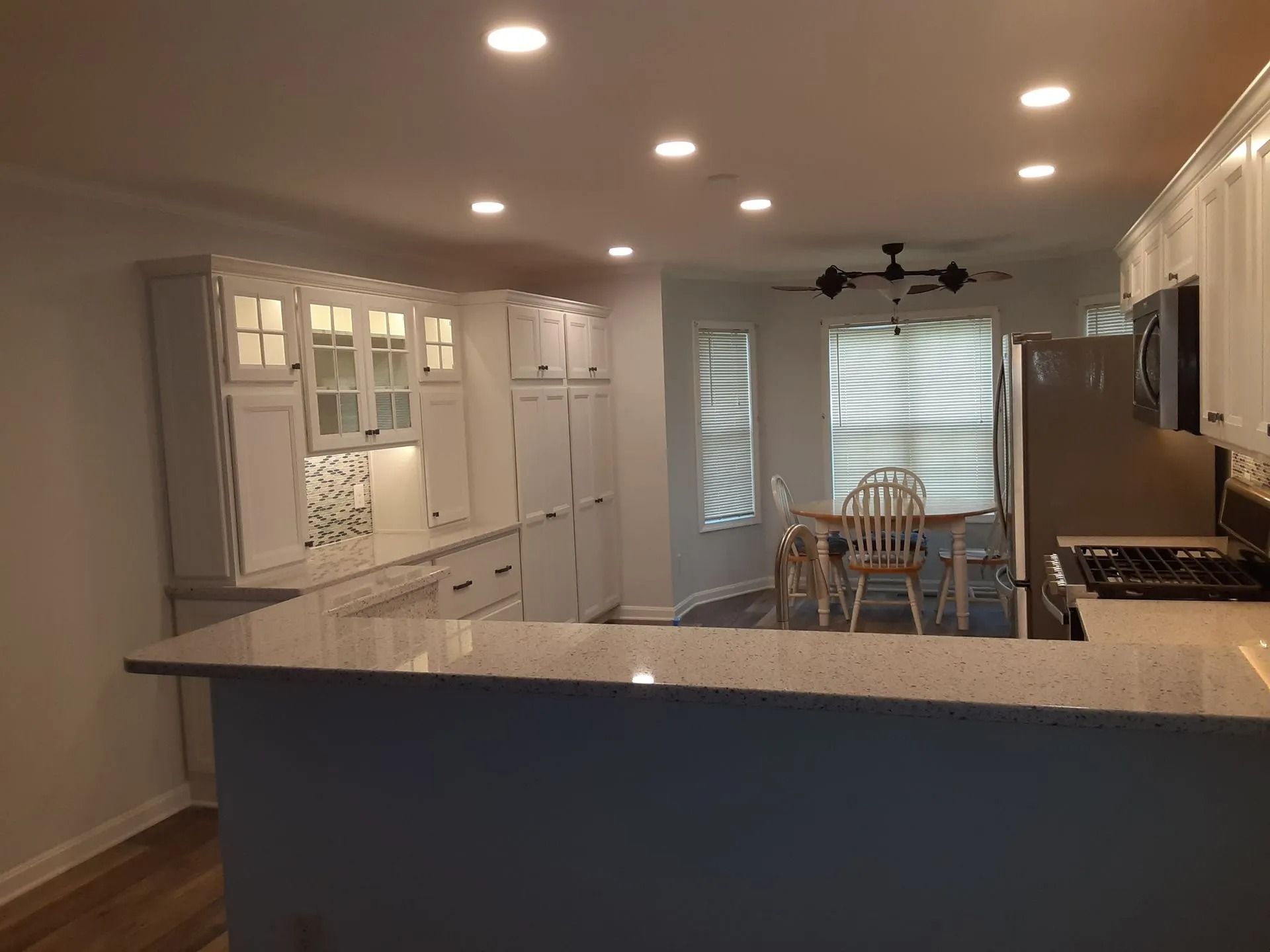Modern kitchen with white cabinets, granite island, and dining area with large windows and chairs