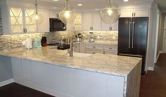 Modern white kitchen with marble island, pendant lights, and stainless steel appliances