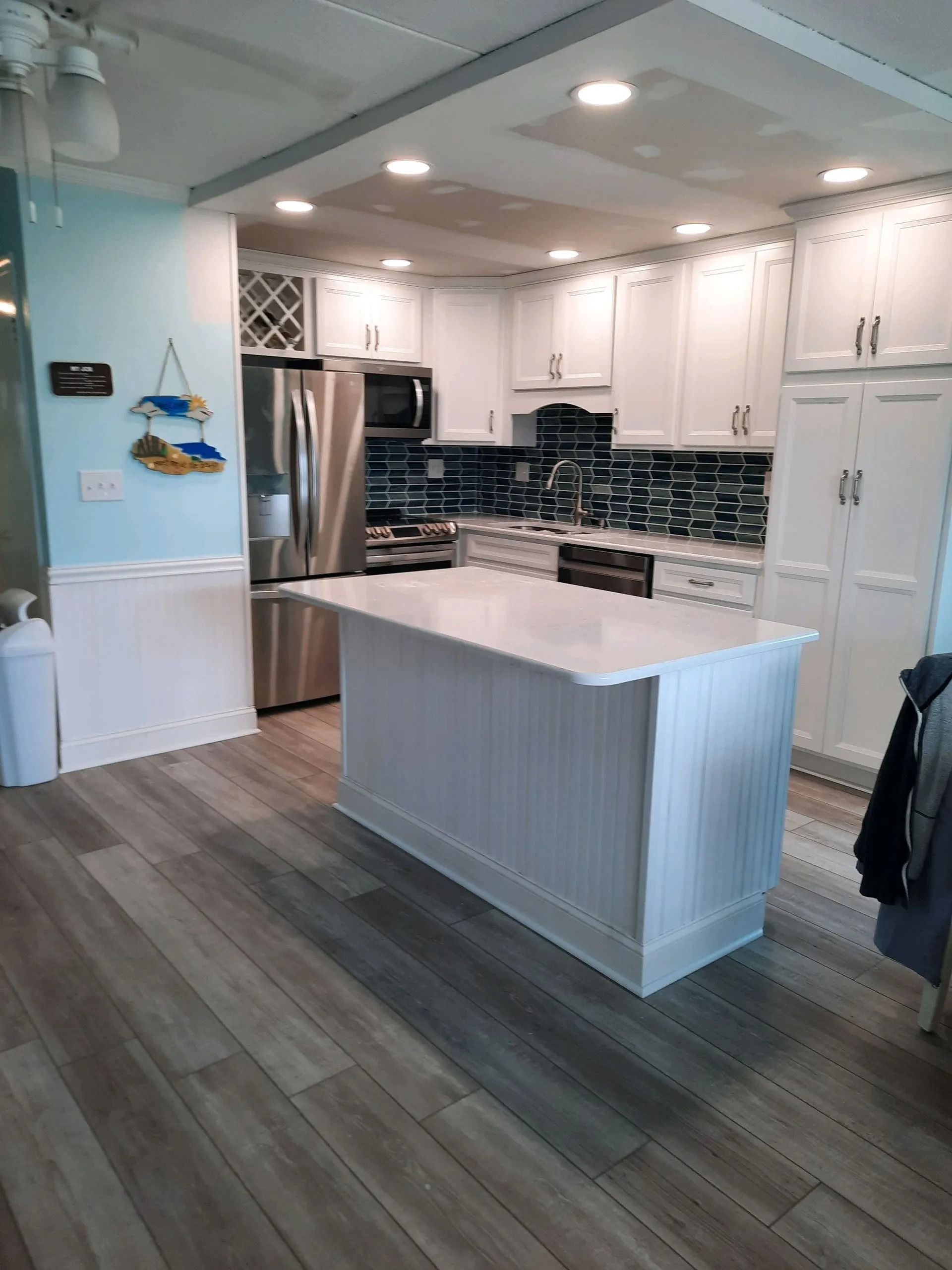 Bright modern kitchen with white cabinets, stainless fridge, and a central island over wood-look flooring