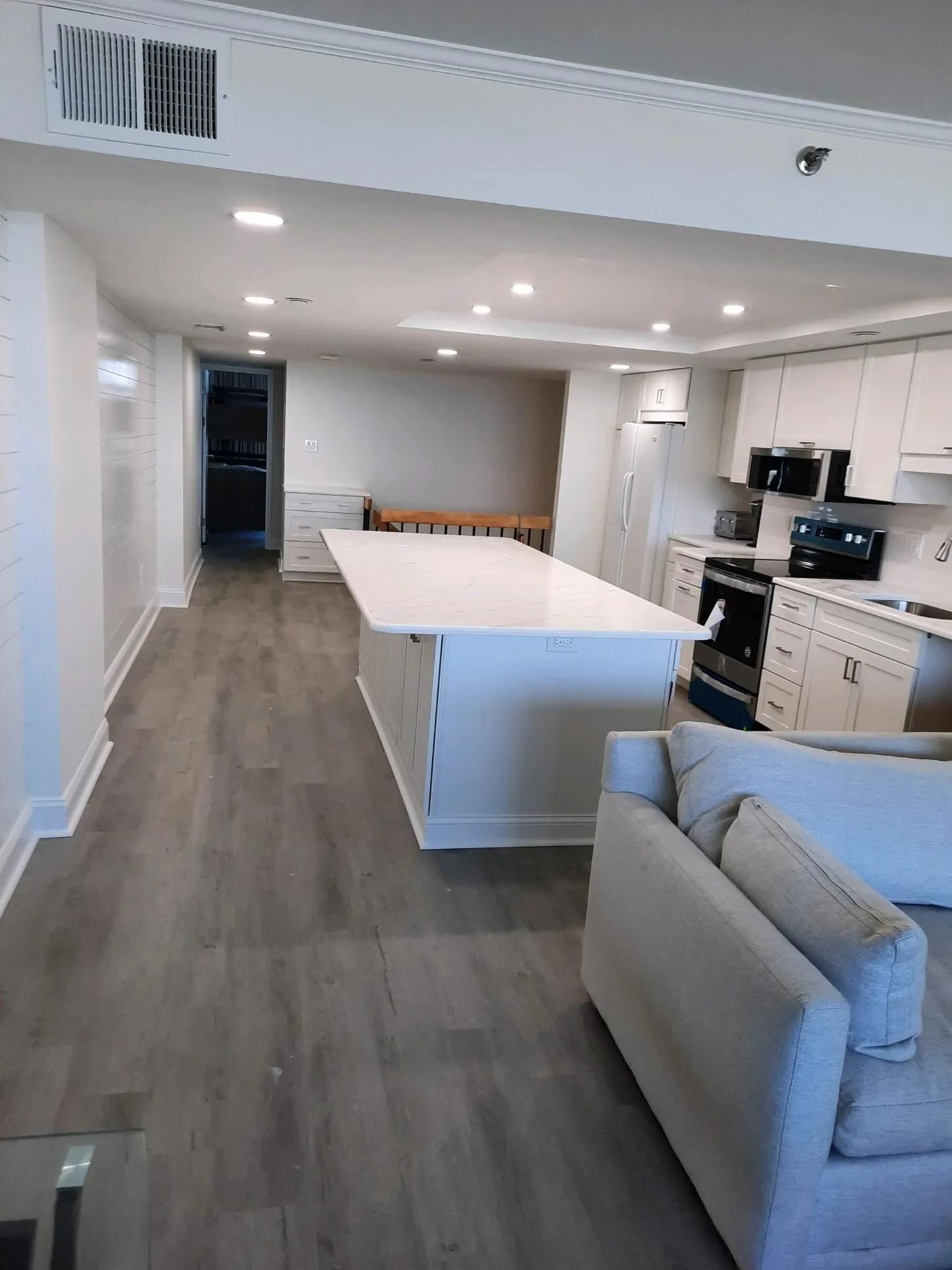 Modern kitchen with white island, gray floors, stainless appliances, and a beige sofa in the foreground