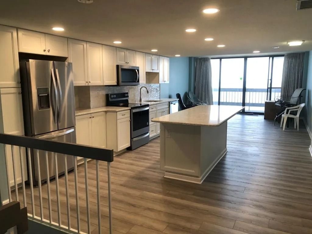 Open kitchen with stainless steel appliances, island, and dining area in a bright modern apartment