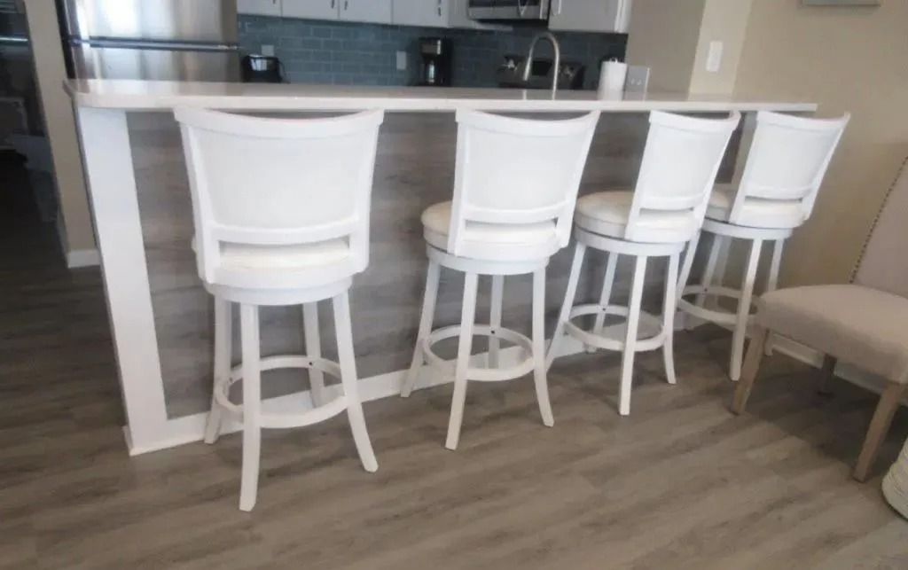 Four white bar stools lined up at a kitchen island in a modern interior