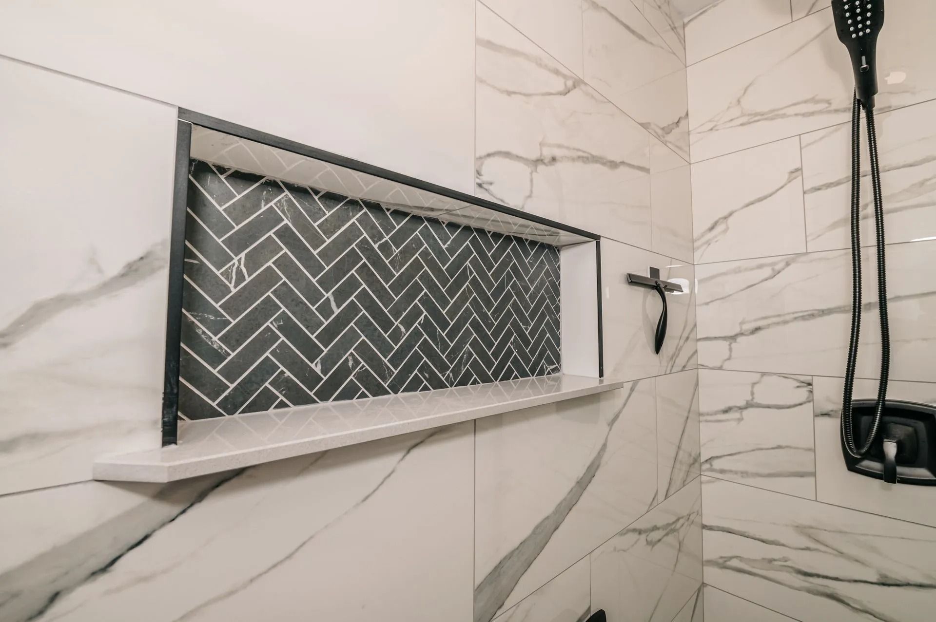 Modern tiled shower with built-in niche, herringbone accent tile, and black shower fixtures