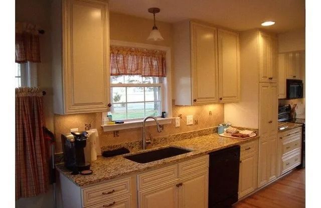 Warm beige kitchen with granite counters, center sink under window, and built-in oven and cabinets