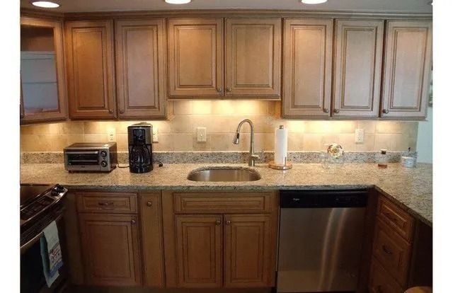 Modern kitchen with wooden cabinets, granite countertop, sink, dishwasher, and small appliances under warm lighting