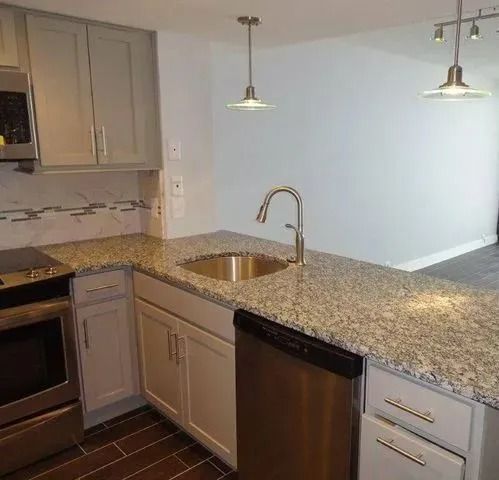 Modern kitchen with granite island, stainless sink and dishwasher, gray cabinets, and two pendant lights