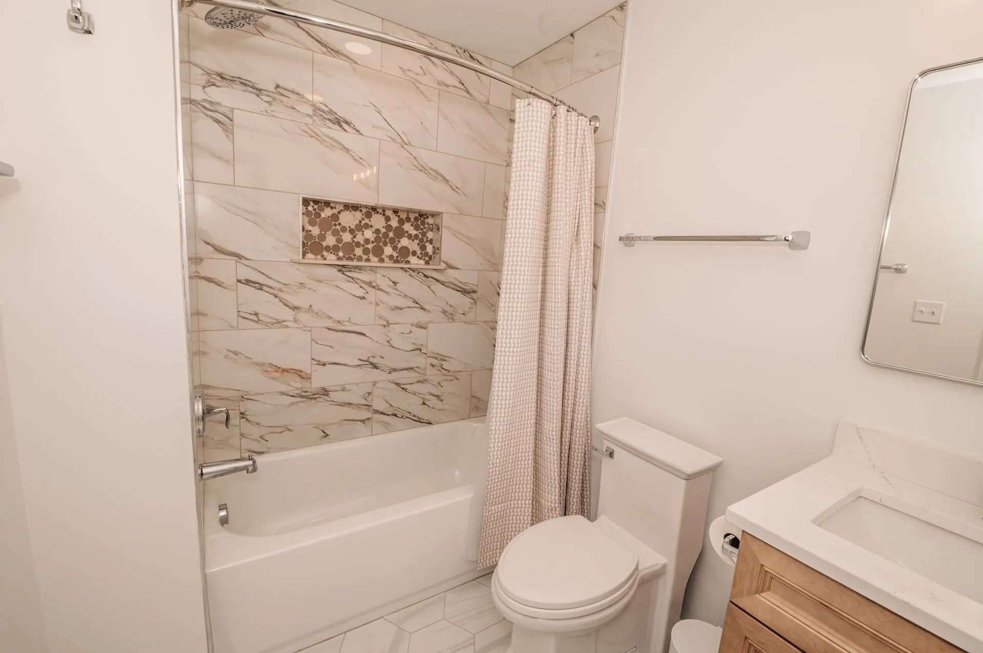 Bright bathroom with a bathtub, toilet, vanity sink, and marble-patterned shower curtain.
