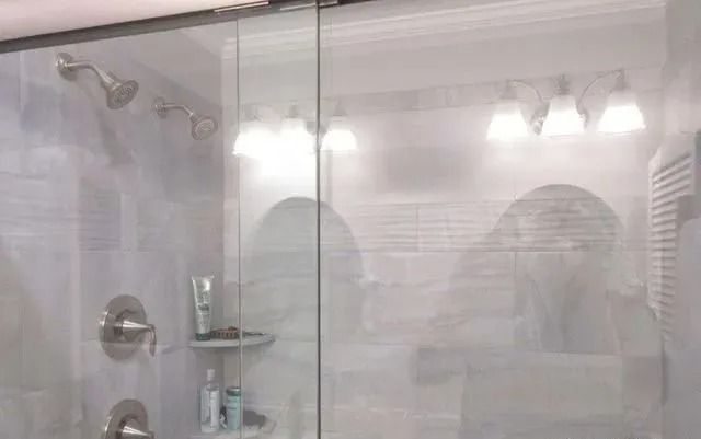 Bright bathroom with glass shower doors, chrome fixtures, and frosted vanity mirrors.