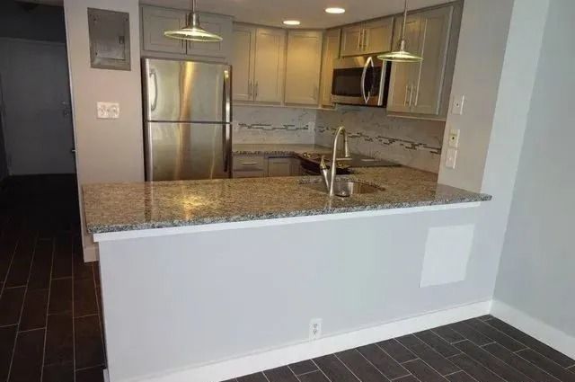 Modern kitchen with granite breakfast bar, stainless steel appliances, and dark tile floor