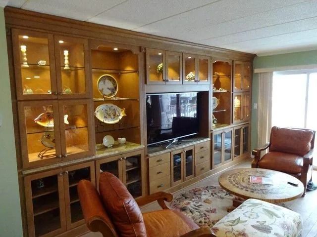 Wooden wall unit with TV, glass cabinets, chairs, and a round coffee table in a bright living room