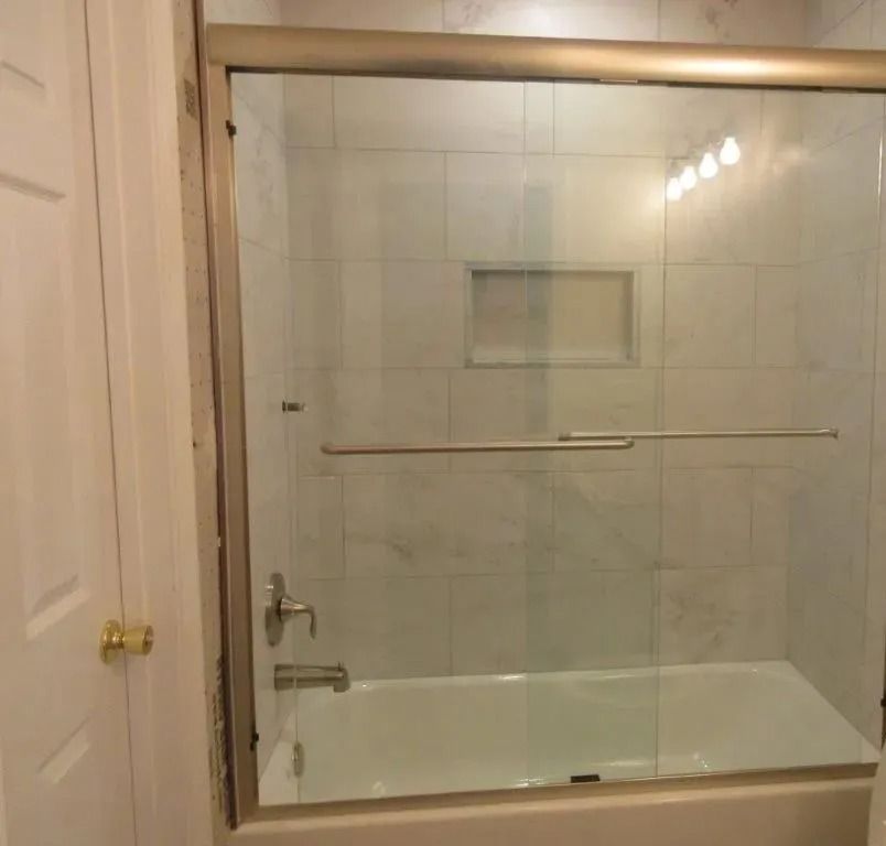 Bathroom bathtub with glass sliding shower doors and tiled wall.