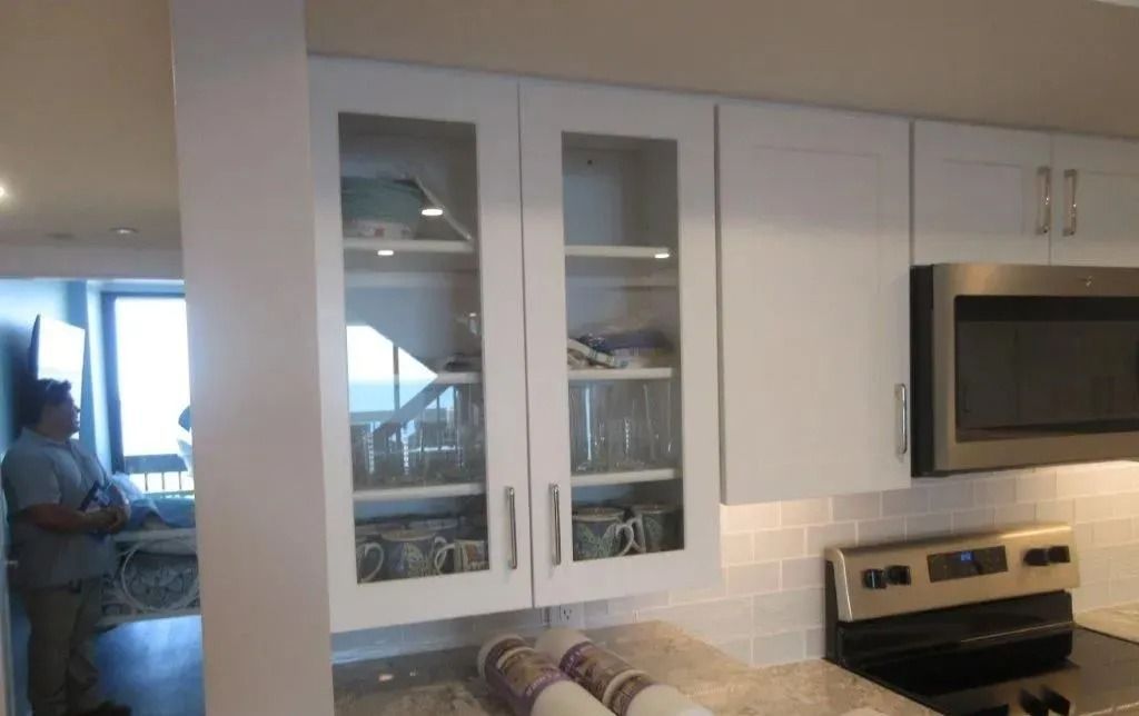 Modern kitchen with white cabinets and stainless appliances; person standing by the window on the left.