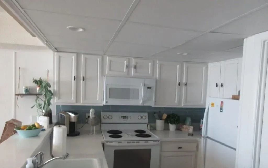 Bright white kitchen with cabinets, stove, refrigerator, and sink countertop.
