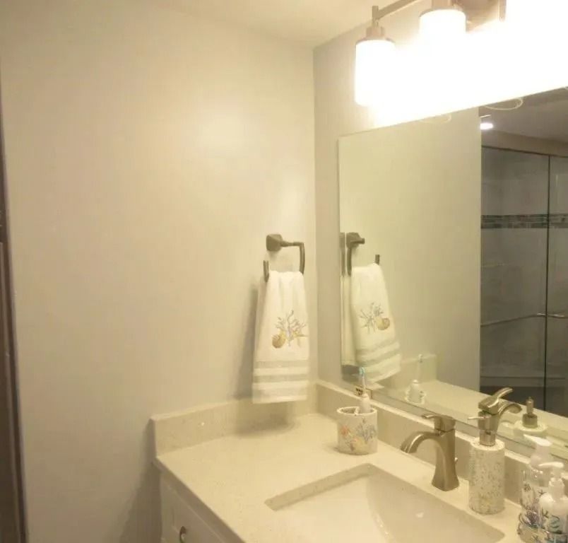 Bathroom vanity with mirror, sink, towel ring, and soap dispensers under a light fixture.