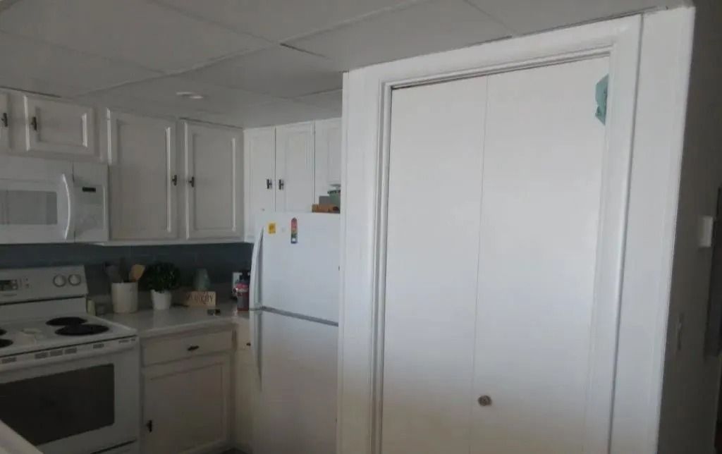 White kitchen with stove, refrigerator, and cabinets next to a closed white closet door