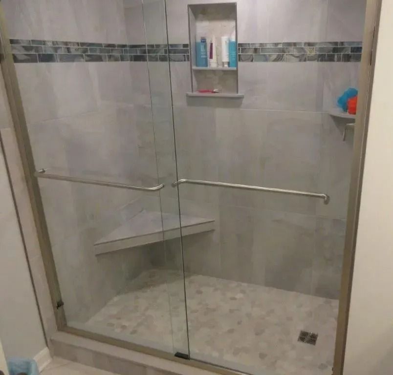 Glass shower enclosure with built-in corner shelf, tile walls, and grab bars in a bathroom