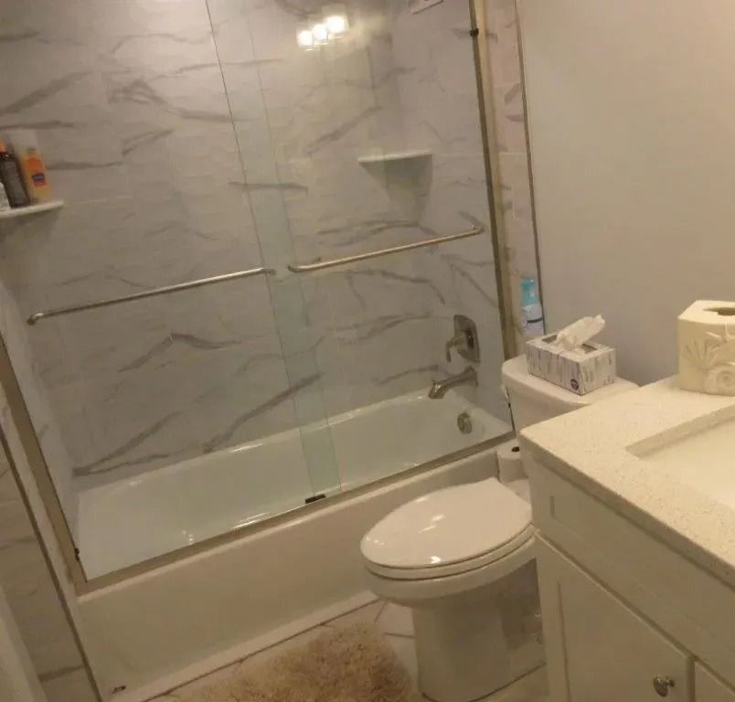 Bathroom with a glass shower, toilet, and white vanity on beige marble tile floor.