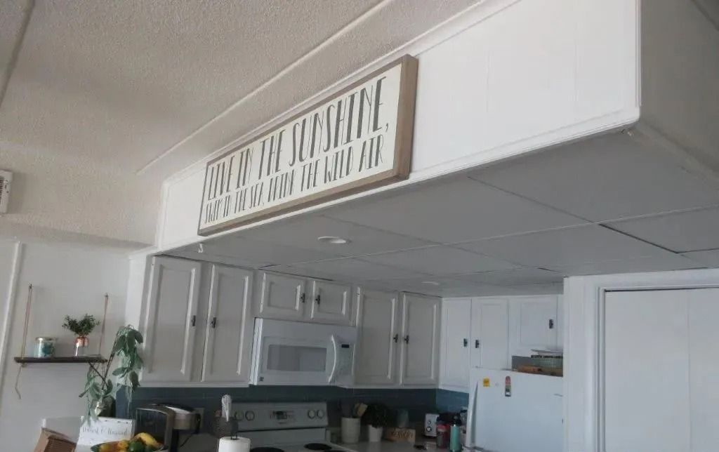 White kitchen with cabinets, refrigerator, and decorative sign above the cabinets.