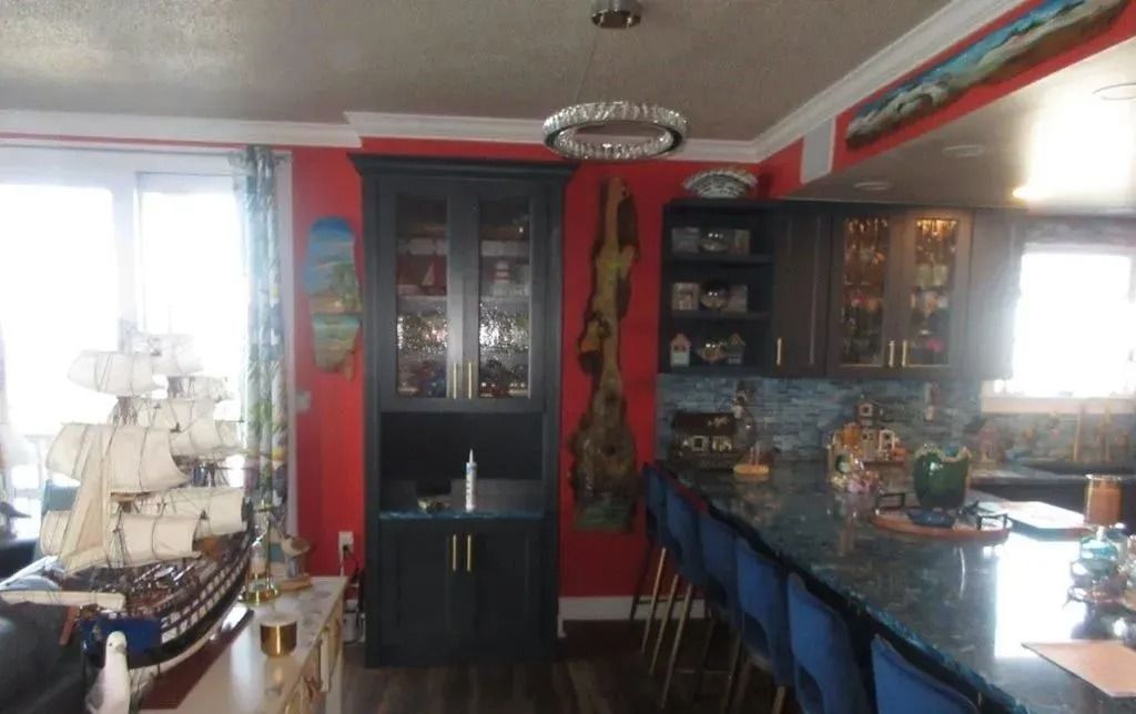 Colorful dining room with red walls, glass cabinet, chandelier, and long blue-covered table by windows