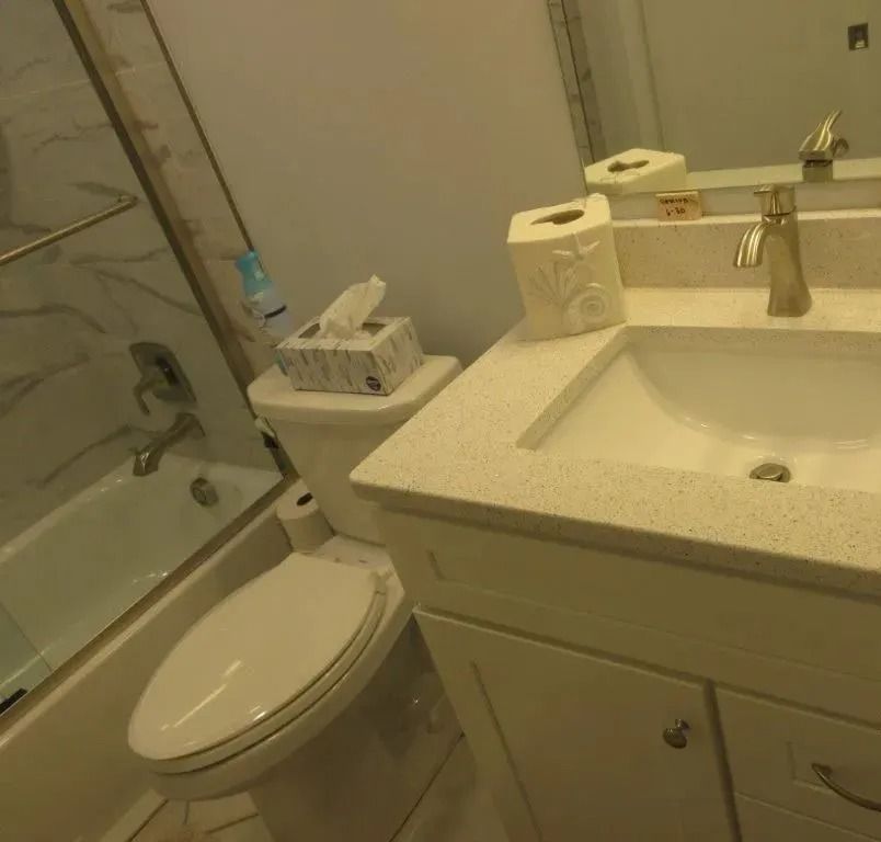 Small bathroom with a sink, toilet, shower, and toiletries on the counter.