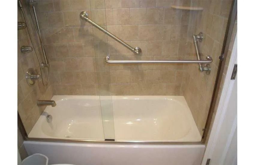 Bathroom with a bathtub, glass shower door, and metal grab bars on tiled walls