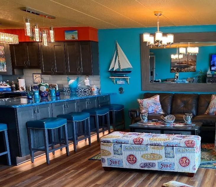 Bright coastal-style living room with turquoise walls, bar stools, sofa, coffee table, and sailboat decor.