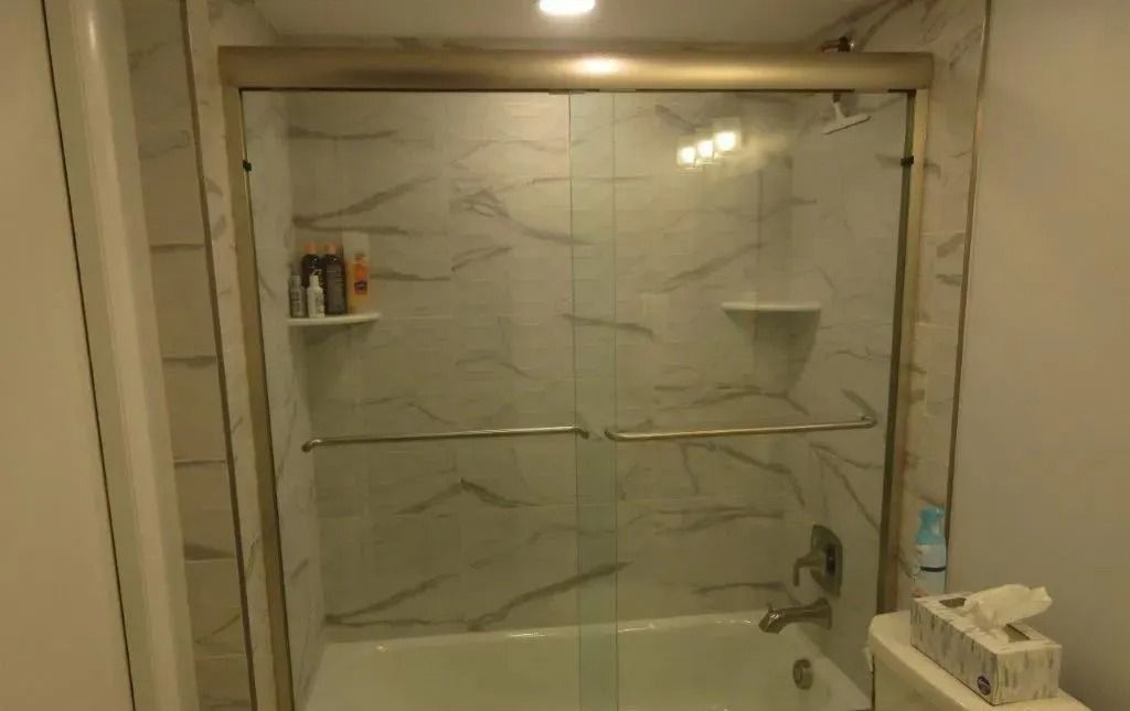 Modern bathroom with a glass-enclosed bathtub/shower and marble-pattern tile walls.