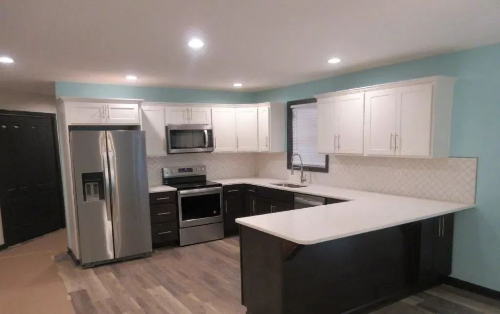 Modern kitchen with stainless appliances, white cabinets, dark countertops, and light blue walls