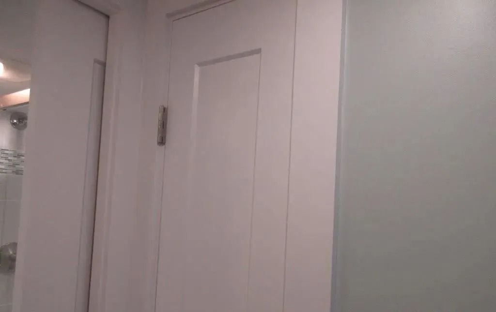 White interior door with a hinge beside a pale wall and frosted glass panel.