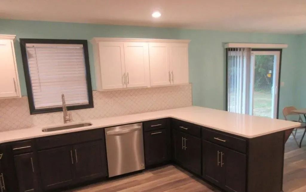Modern kitchen with dark cabinets, white countertops, stainless dishwasher, and windows overlooking greenery