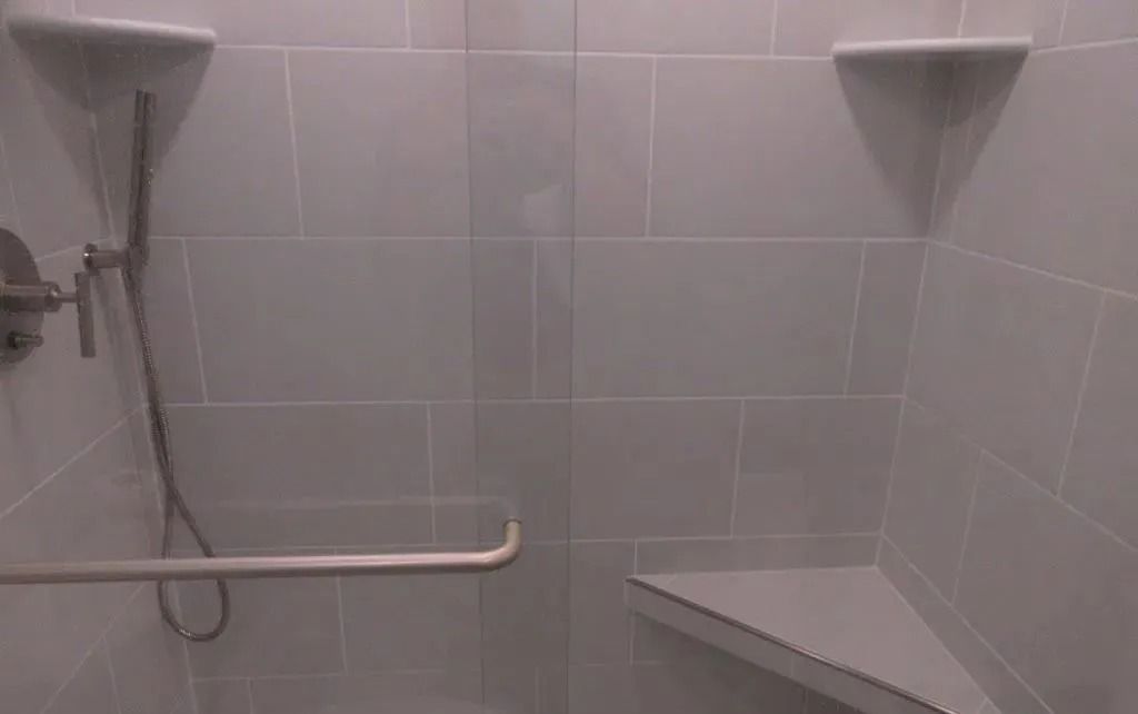 Accessible shower room with wall-mounted seats, grab bars, and a handheld showerhead.