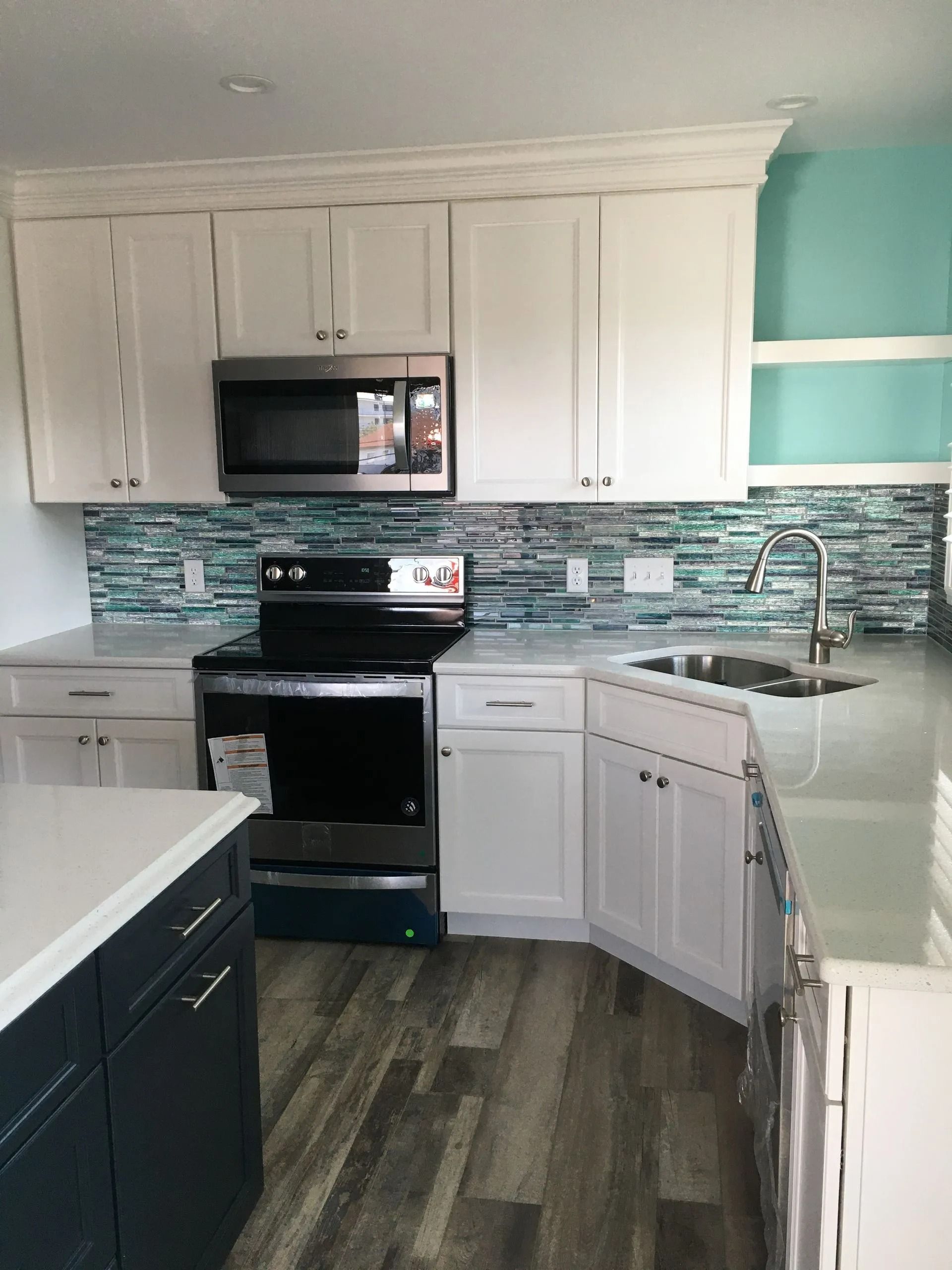 Modern kitchen with white cabinets, black stove, mosaic tile backsplash, and teal accent wall