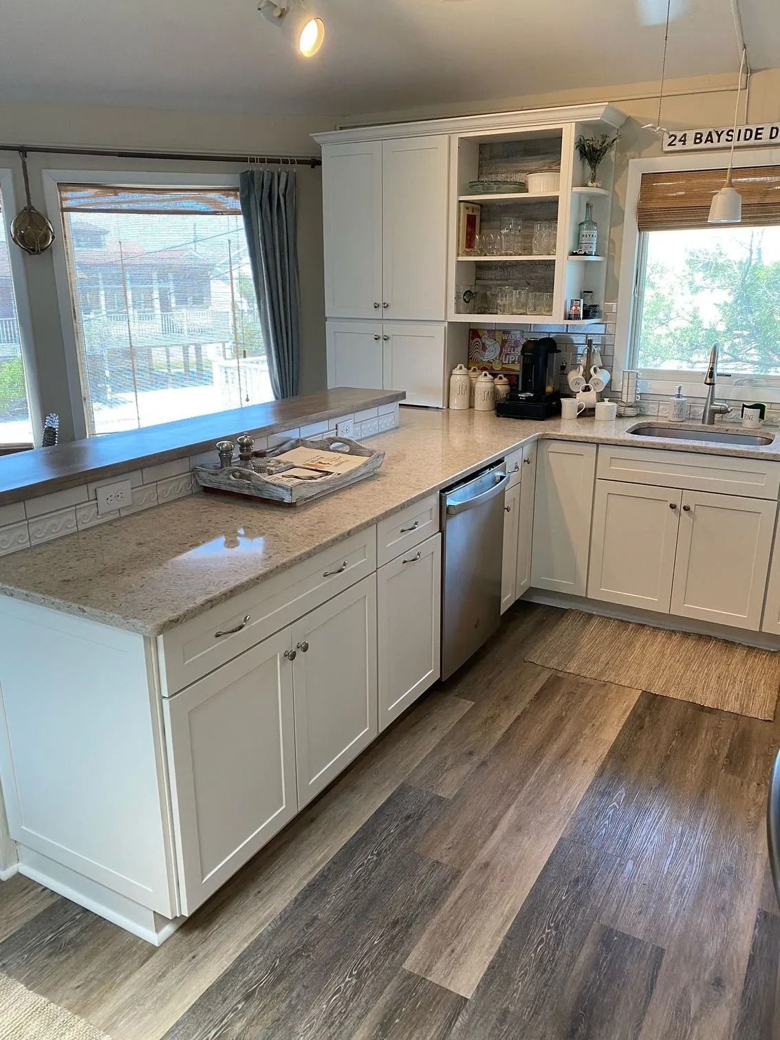 Bright white kitchen with gray countertops, wood floor, and large windows letting in daylight