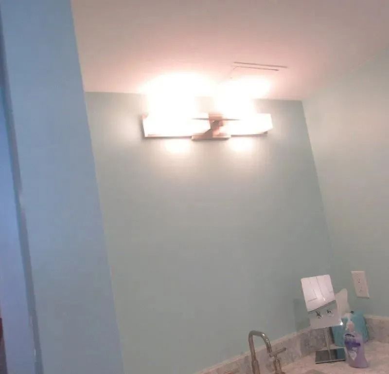 Bathroom wall with bright vanity light above a sink and countertop with toiletries.