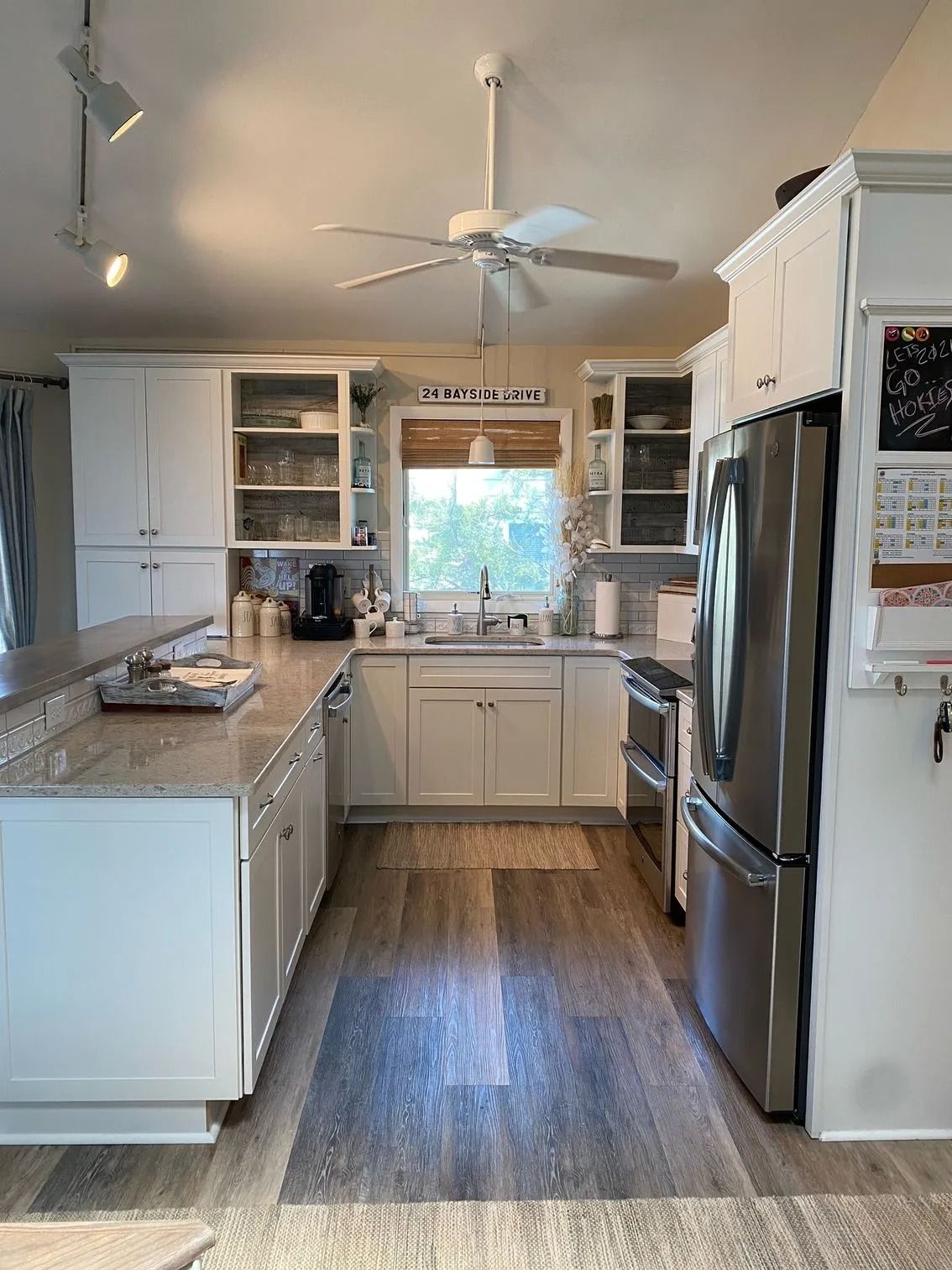 Modern white kitchen with island, stainless steel appliances, ceiling fan, and window over the sink