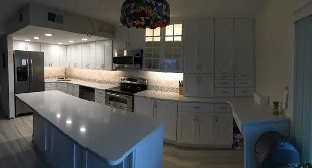 Bright modern kitchen with white cabinets, a large island, and under-cabinet lighting at dusk.