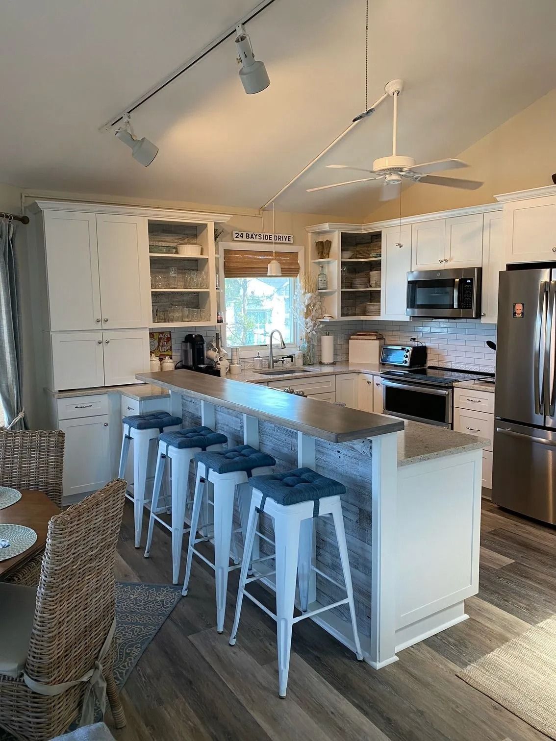 Bright kitchen with white cabinets, large island, bar stools, and stainless steel appliances under track lighting