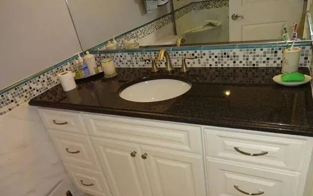 Bathroom vanity with white cabinets, dark countertop, oval sink, and wall mirror under staircase.