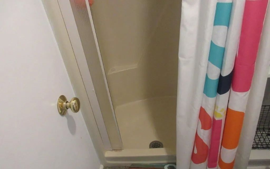 White shower stall with brass handle and colorful striped shower curtain partially open
