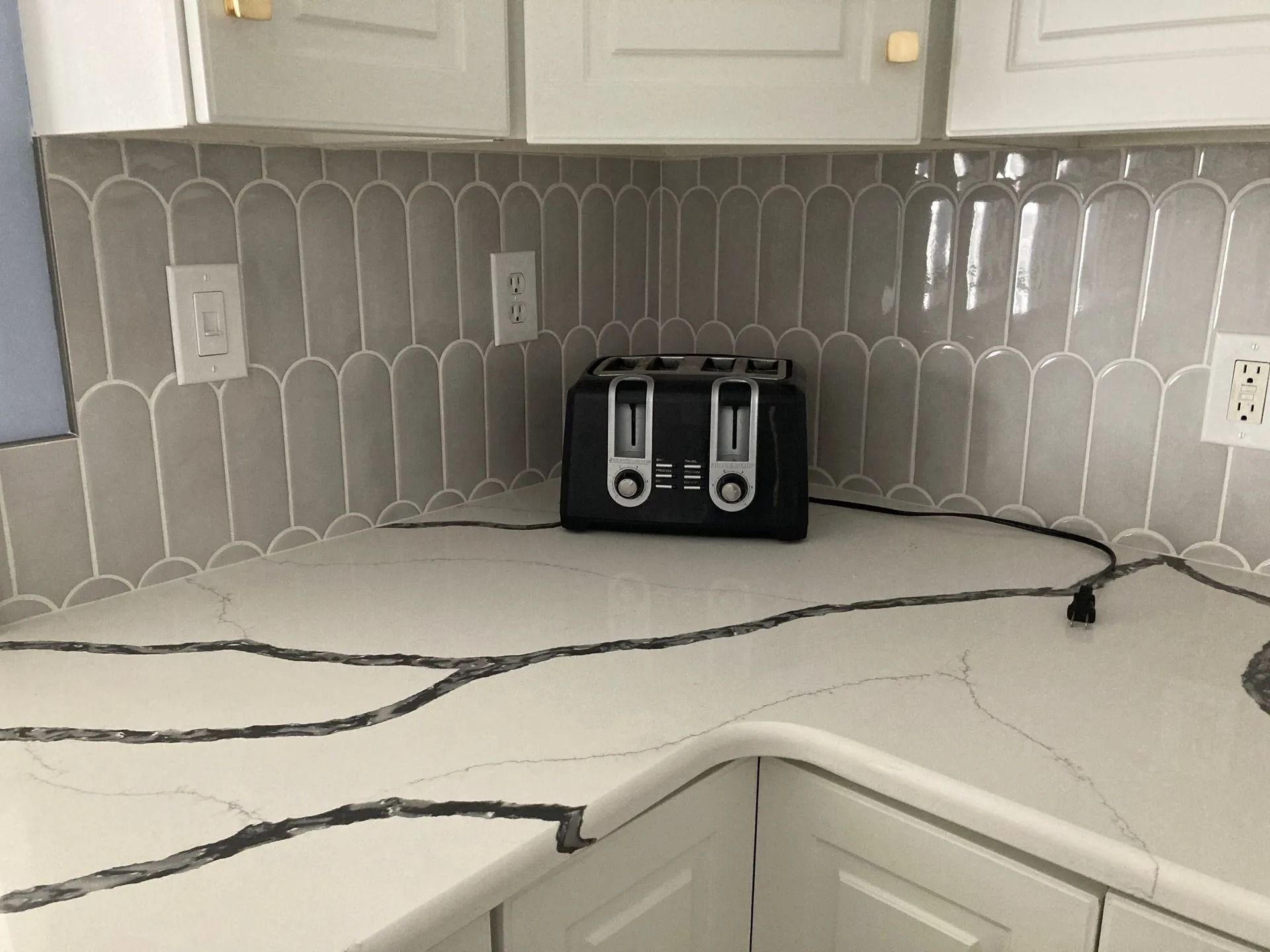 Black toaster on a white kitchen countertop with cracked marble-like surface and tiled backsplash