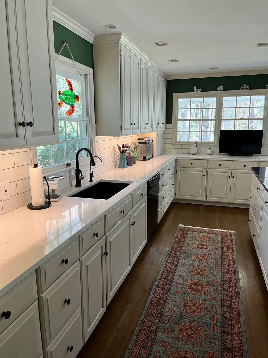 Bright kitchen with white cabinets, black countertops, a sink by the window, and a patterned runner rug.