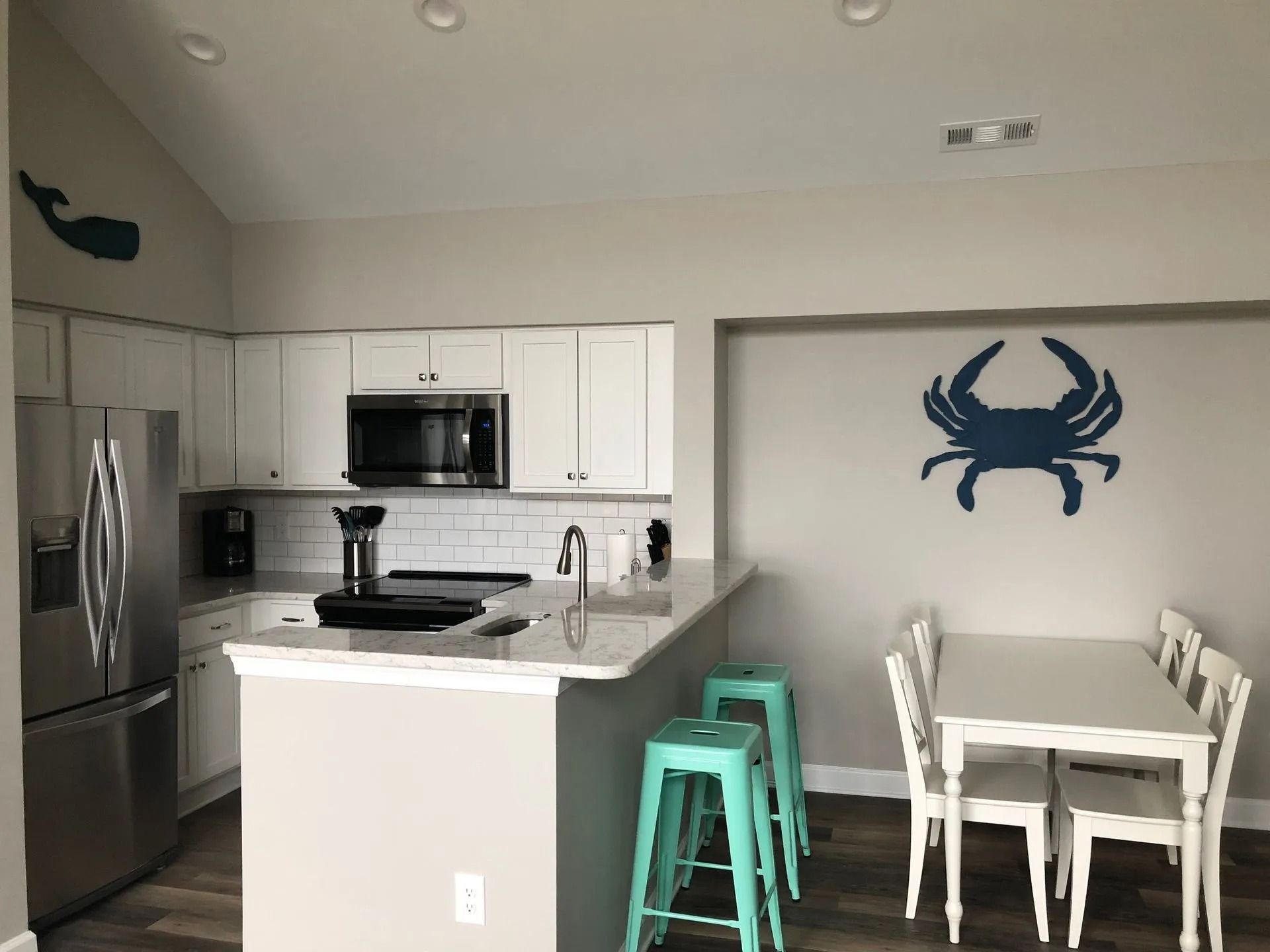 Modern kitchen and dining area with stainless steel appliances, mint stools, and a blue crab wall decoration